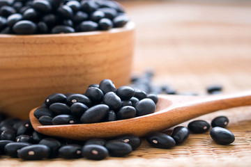 Raw black beans in wooden bowl and spoon on table.