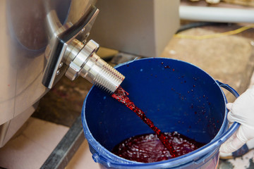 The red liquid flows into a blue plastic bucket. Confectionery. Metal tank with liquid. Making...