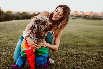 .Young and smiling woman playing with her brown spanish water dog wrapped in a gay flag, proud of her sexual orientation. Fighting for rights and freedoms. Lifestyle