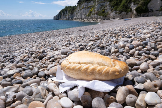 Cornish Pasty On Shingle Beach With Sea In Background