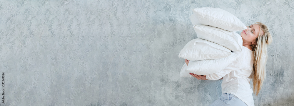 Wall mural Happy housewife. Morning chores. Woman holding pile of pillows on gray background. Copy space.