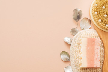 Body skin care and hygiene. Cropped top view of wooden body brush, organic loofah and handmade soap. Peach background. Copy space.