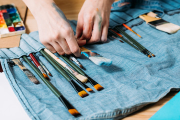 Painter kit. Closeup of artist hands choosing paintbrush. Handmade denim bag organizer.