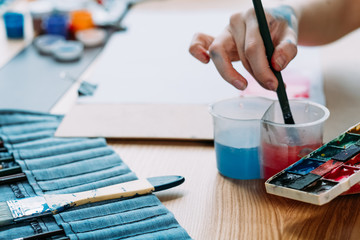 Art school. Closeup of artist hand washing brush. Painter using watercolor palette.