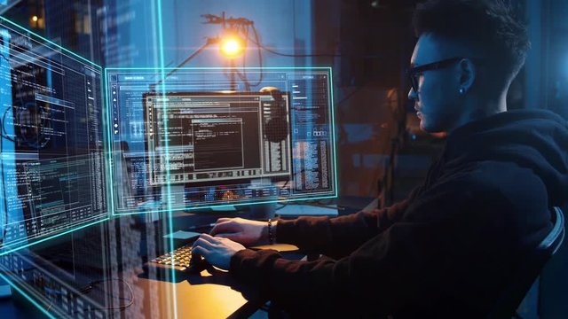 cybercrime, hacking and technology concept - asian male hacker in dark room writing code or using computer virus program for cyber attack