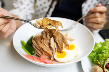 woman holding sliced roasted duck meat on spoon, ready to eat