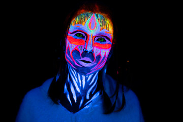 Close-up Portrait of Young naked bodyarted woman in blue glowing ultraviolet paint and Yellow eye lenses. Avatar entity amazon warrior girl with pigtails hairstyle