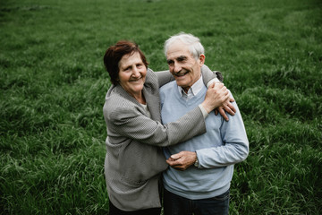 Fototapeta premium Happy smiling senior couple in love on nature, having fun. Elderly couple on the green field. Cute senior couple walking and hugging in spring forest
