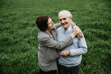 Happy smiling senior couple in love on nature, having fun. Elderly couple on the green field. Cute senior couple walking and hugging in spring forest