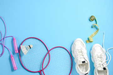 Sports flat lay with shuttlecock and badminton racket, skipping rope, sneakers and measuring tape on blue background. Fitness, sport and healthy lifestyle concept.