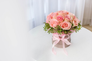 Beautiful bouquet of pink roses in a festive round box on a white table. Gift for holiday, birthday, Wedding, Mother's Day, Valentine's day, Women's Day.  Flowers in a hat box.