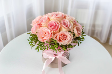 Beautiful bouquet of pink roses in a festive round box on a white table. Gift for holiday, birthday, Wedding, Mother's Day, Valentine's day, Women's Day.  Flowers in a hat box.