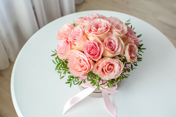 Beautiful bouquet of pink roses in a festive round box on a white table. Gift for holiday, birthday, Wedding, Mother's Day, Valentine's day, Women's Day.  Flowers in a hat box. Top view.