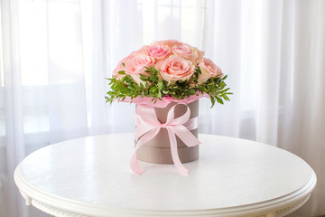 Beautiful bouquet of pink roses in a festive round box on a white table. Gift for holiday,...
