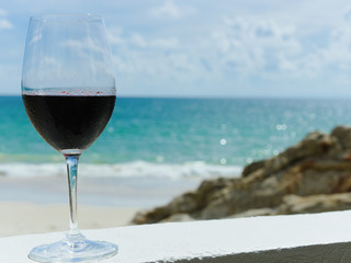 Romantic glass of chilled red wine, on the background the beach and azure sea. blurred background