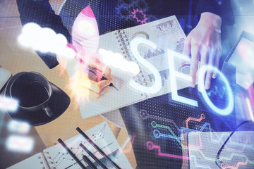 Double exposure of woman's hands making notes with SEO icon. Concept of Search engine optimization