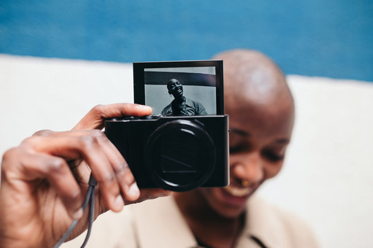 African woman holding a digital camera that shows her portrait smiling