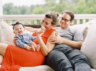 Mom and Dad snuggling while young daughter laughs on porch