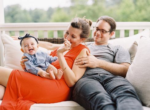 Mom and Dad snuggling while young daughter laughs on porch