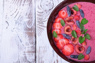 Berry smoothie bowl topped with strawberries, cherries, honeysuckles and mint
