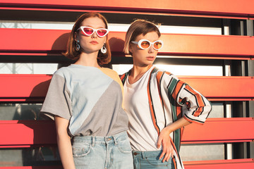 Two young women standing near red  backgroung in city under sun light.