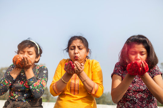 Mother and two daughters blowing color powder at outdoors