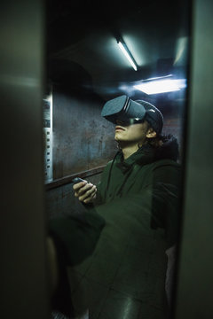 Young man using gray VR goggles finding himself in an industrial elevator