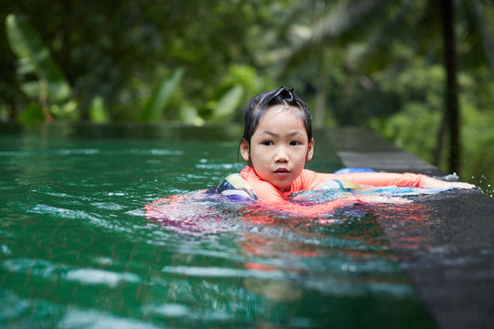 Cute Asian girl playing in an infinity pool with mandala scarves in the woods of nature