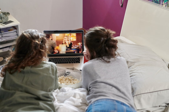 Women lounging on bed with laptop and popcorn