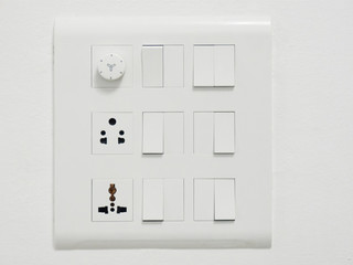 Twelve electrical white switches, two sockets and a dimmer on a white wall