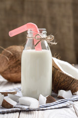 Glass bottle of milk or yogurt on blue napkin on white wooden table with coconut aside