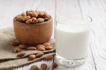 Milk or yogurt in drinking glass on white wooden table with bowl of almonds on hemp napkin aside
