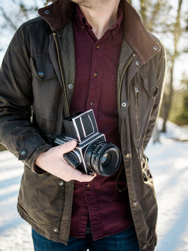 A man in a green jacket stands in the snow with an old camera.