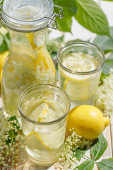 Elderflower Lemonade.  Lemonade with elderflower and lemons, a delicious and refreshing homemade cold drink in glasses and a carafe on a white wooden table.