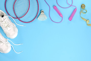 Sports flat lay with shuttlecock and badminton racket, skipping rope, sneakers and measuring tape on blue background. Fitness, sport and healthy lifestyle concept.