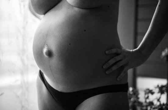 Black and white shot of a topless pregnant woman 's baby bump