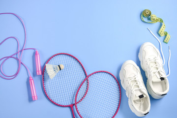 Sports flat lay with shuttlecock and badminton racket, skipping rope, sneakers and measuring tape on purple background. Fitness, sport and healthy lifestyle concept.