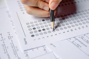 Students hand holding pencil writing selected choice on answer sheets and Mathematics question sheets. students testing doing examination. school exam