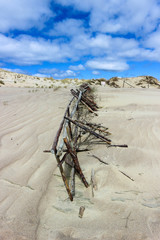 sand-covered old coastal dune fence under blue sky with clouds