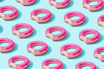 Trendy sunlight Summer pattern made with pink doughnut inflatable toy on bright light blue background. Minimal summer concept.
