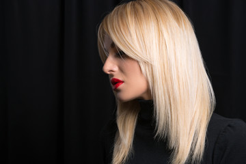 Sexy and beautiful model with direct blond hair on black background. Lips painted with red lipstic.