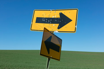 Bullet holes covering directional arrow signs, rural farmland in distance, Palouse, Washington