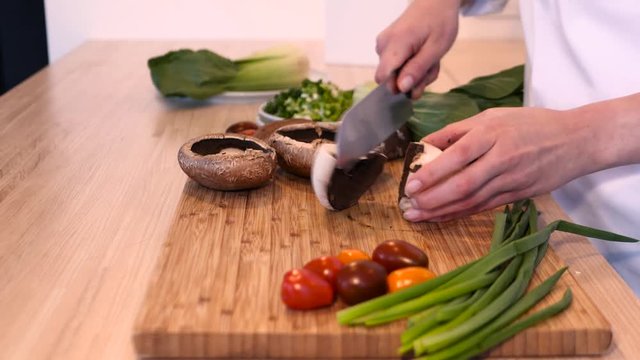 chef cutting big mushrooms with vegetables in background