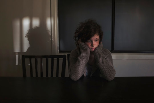 Quiet girl sitting at table in shadows