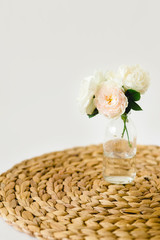 Beautiful roses in glass vase on a wicker napkin on white background