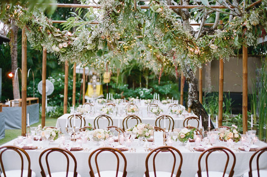 Outdoor, tropical wedding reception with hanging greenery garlands