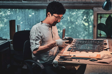Diligent restorer in glasses is counting right amount for stained glass at his own workshop.