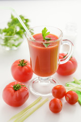 Tomato juice is poured into a transparent glass with parsley and herring, on a white background with cherry tomatoes, lit by sunlight