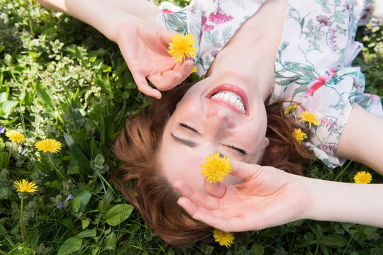 Woman lying in the grass, playfully holding dandelions