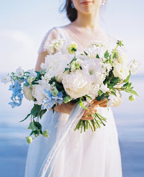 Crop bride with bouquet near sea